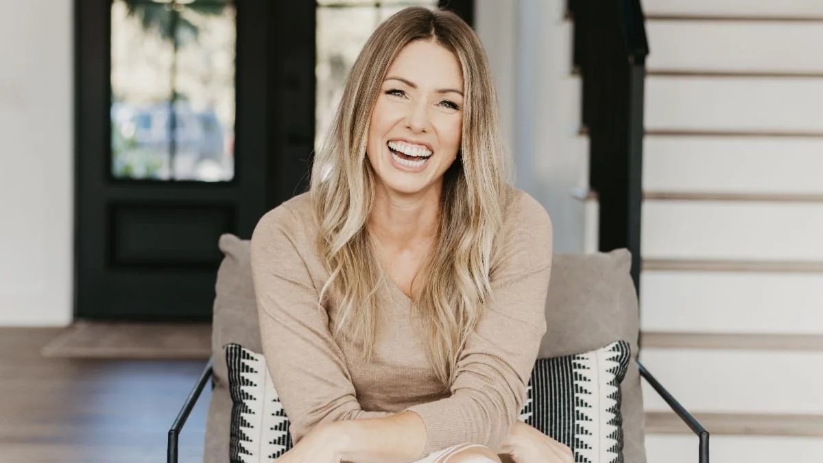Melissa Perry laughing, seated in a beige sweater